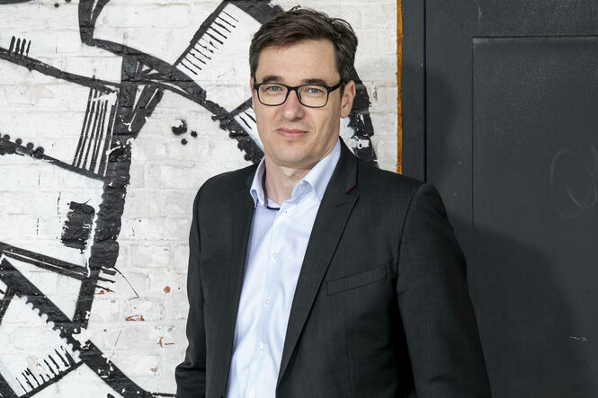 Ein Mann im Anzug steht vor einer mit Graffity besprühten Wand