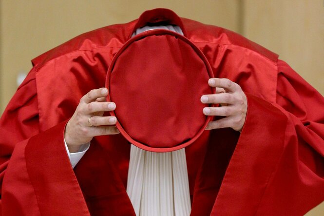 Richter in roter Robe setzt den Hut auf
