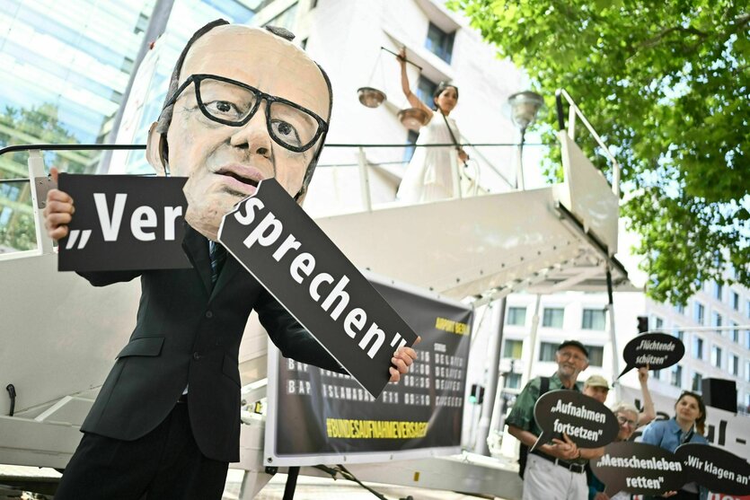Ein Aktivist mit Merz-Maske zerbricht während einer symbolischen Protestaktion ein Schild mit der Aufschrift „Versprechen“