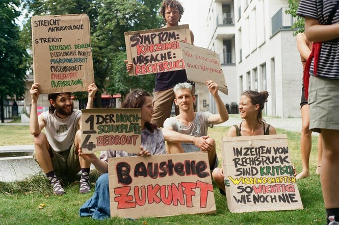 Studierende sitzen mit Plakaten auf einer Wiese