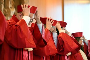 Die Richter:innen in roten Roben heben ihre roten Hüte