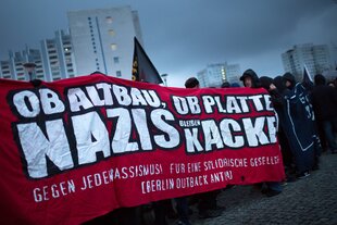 Demonstranten laufen im Plattenbau mit Banner: 