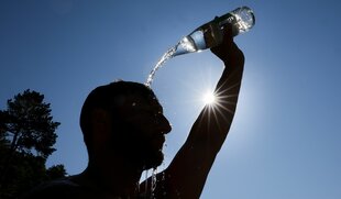 Ein Mann kühlt sich bei sommerlichen Temperaturen ab, in dem er sich eine Flasche mit Wasser über den Kopf schüttet