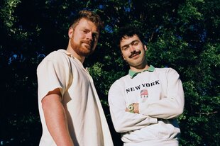 Die Brüder Dana und Alden lächeln vor Bäumen in der Sonne in die Kamera.