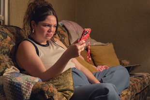 Eine Frau sitzt auf der Couch und schaut auf ihr Handy