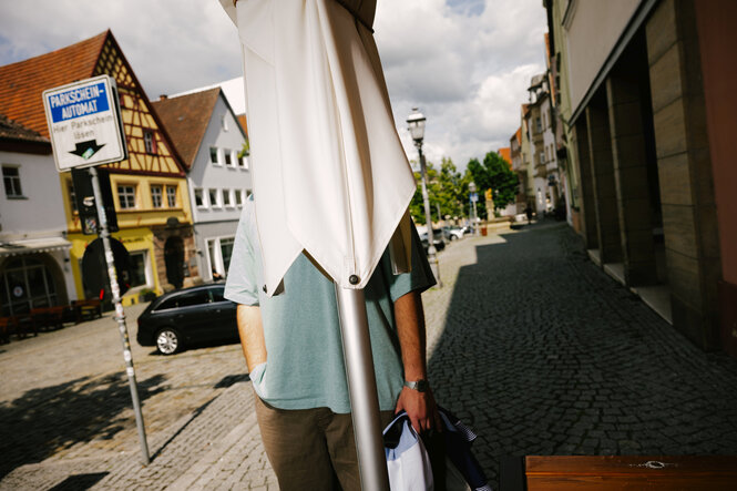 Daniil steht verdeckt unter einem Sonnenschirm auf einem Gehweg