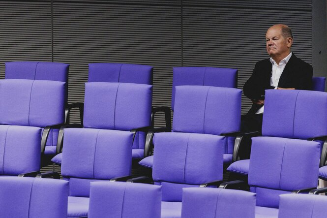 Olaf Scholz sitzt mit verschränkten Armen und grimmigen Blick mutterseelenallein in der hintersten Reihe im Bundestag