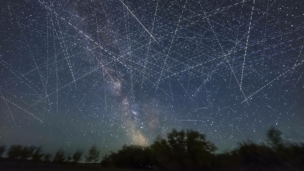 Eine langzeitbelichtete Nachtaufnahme zeigt einen Sternenhimmel an dem Satelliten kreisen