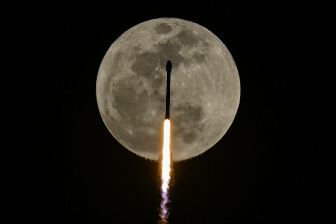 Eine Rakete bewegt sich vor dem Vollmond in den Himmel. Ein Feuerschwall kommt aus ihrem Heck