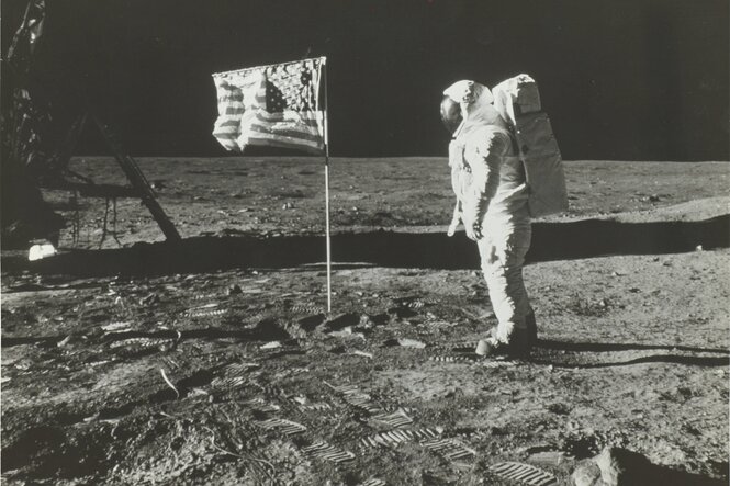 Ein Astronaut im Raumanzug steht neben einer US-Fahne auf dem Mond