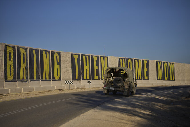 Ein Fahrzeug der israelischen Armee nahe der Grenze zu Gaza neben einem Transparent, auf dem „Bring them home now" steht