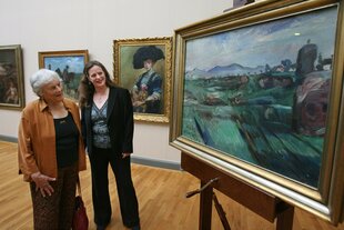 Zwei Personen stehen in einem Museum vor Gemälden, darunter ein Porträt einer Frau mit Hund und ein Landschaftsbild.