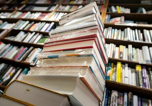 Ein Stapel Bücher, im Hintergrund ein volles Bücherregal