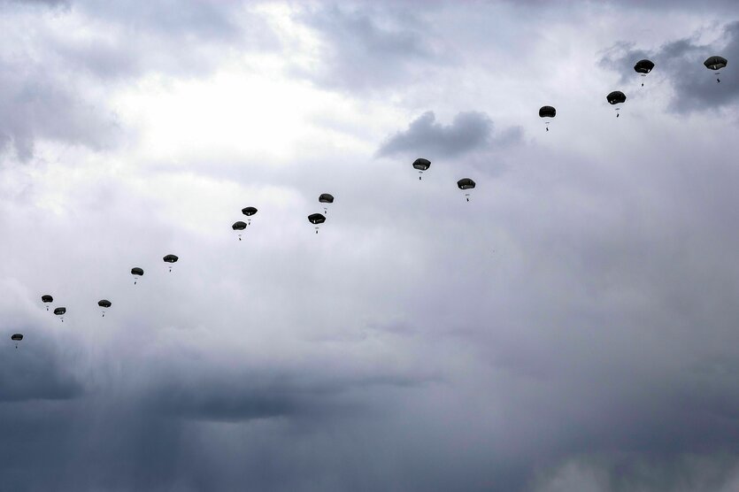 Eine lange Reihe von Fallschirmspringern fliegt vor einem grau verhangenen Himmel nach unten