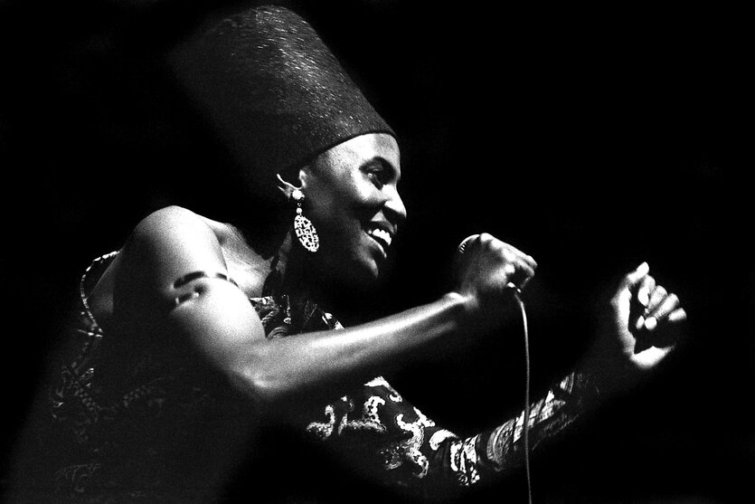 Porträt von Miriam Makeba, sie hält ein Mikrofon inder Hand, lacht und singt