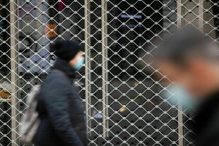 Menschen mit Mundschutz gehen an einem geschlossenen Geschäft vorbei