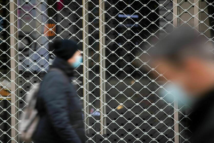 Menschen mit Mundschutz gehen an einem geschlossenen Geschäft vorbei