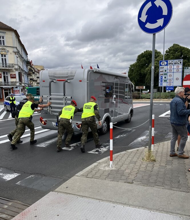 Polnische Grenzschützer schieben einen liegen­gebliebenen Wohnwagen nach Słubice