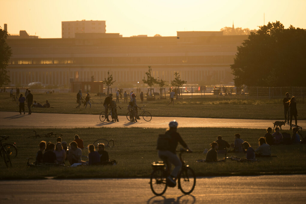 Menschen sitzen vor Sonnenuntergang auf dem Temepelhofer Feld in Berlin