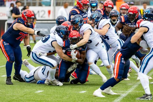 Ein American-Football-Spiel mit einer intensiven Szene, in der Spieler in roten und blauen Uniformen um den Ball kämpfen.