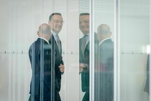 Jens Spahn, herablassend und hämisch lächelend, durch mehrere Glasreflektionen gesehen, kommt zur Fraktionssitzung der Unionsparteien vor der Wahl von Richtern
