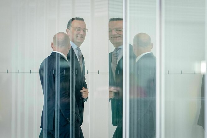 Jens Spahn, herablassend und hämisch lächelend, durch mehrere Glasreflektionen gesehen, kommt zur Fraktionssitzung der Unionsparteien vor der Wahl von Richtern
