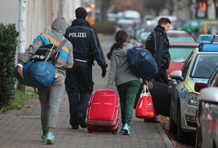 Menschen mit Koffern werden von Polizisten begleitet