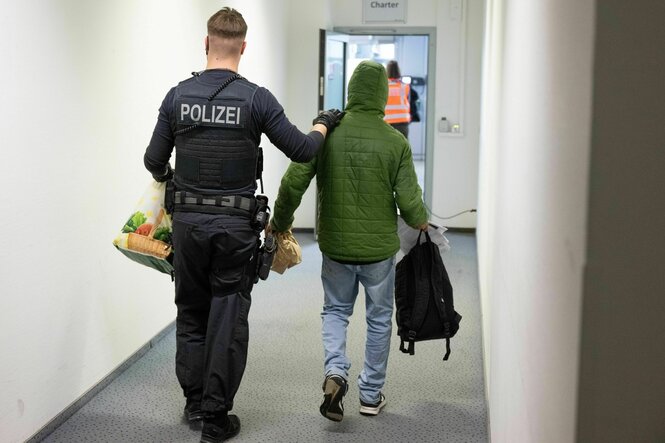 Ein Polizeibeamter bringt einen Mann zu einem Abschiebeflug, wir sehen sie von hinten