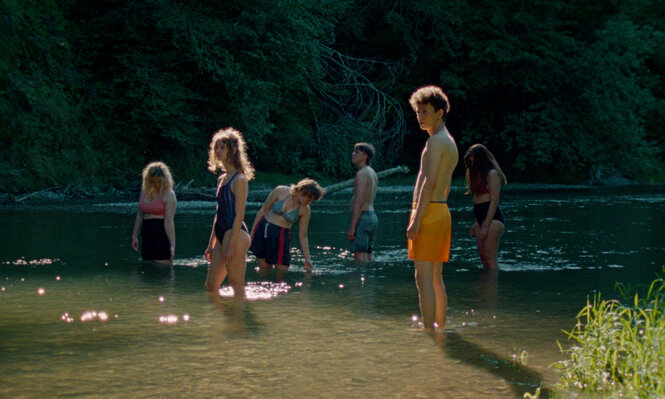 Jugendliche stehen angezogen bis zu den Knöcheln im Seewasser
