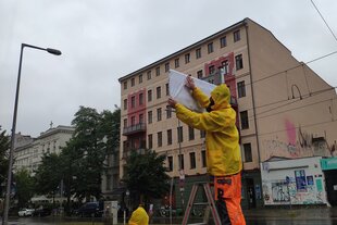 Ein Mitarbeiter des Bezirksamtes Pankow enthüllt am Samstag bei starkem Regen ein neues Straßenschild am Jahnsportpark