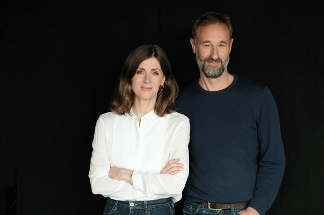 Ein Porträtfoto von der taz-Chefs Aline Lüllmann und Andreas Marggraf. Aline Lüllmann, links im Bild, trägt eine weiße Bluse und Jeans, ihre Arme sind verschränkt. Andreas Marggraf, rechts im Bild, hat einen Bart und trägt ein dunkles Langarmshirt und Jeans. Beide blicken direkt in die Kamera vor einem dunklen Hintergrund.