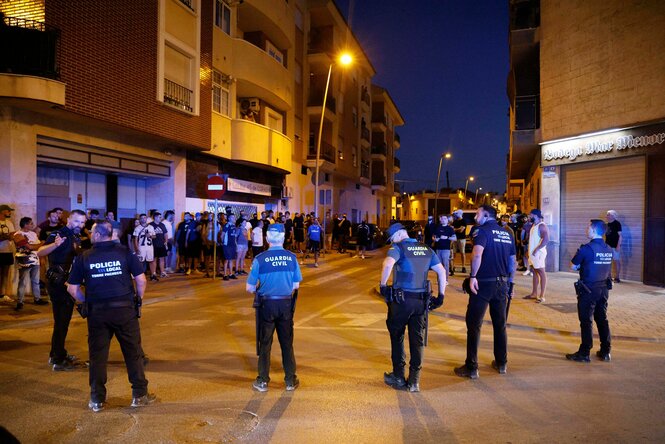 Eine Kreuzung bei Nacht. Im Vordergrund stehen Polizisten im Halbkreis, dahinter Zivilpersonen