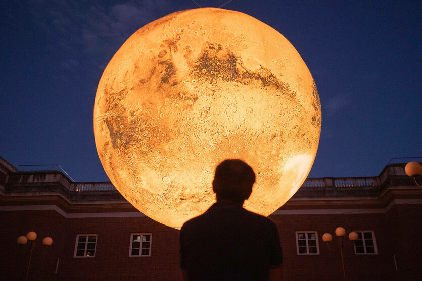 Eine Person steht Nachts vor einem großen Modell vom Mars