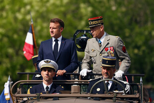 Präsident Macron steht bei einer Parade auf einem Fahrzeug.