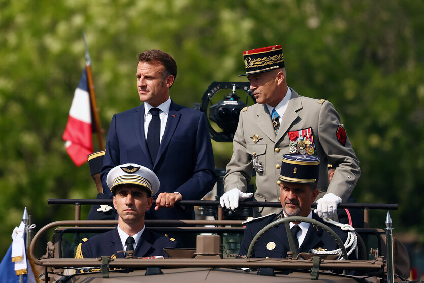 Präsident Macron steht bei einer Parade auf einem Fahrzeug.