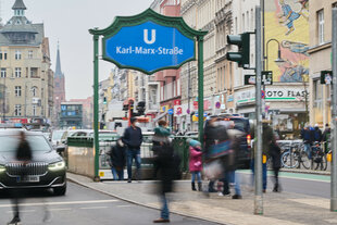 Personen gehen an der U-Bahn Station Karl-Marx-Straße über die Straße