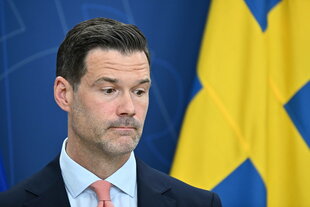 Ein Mann steht vor einer schwedischen Flagge und schaut skeptisch