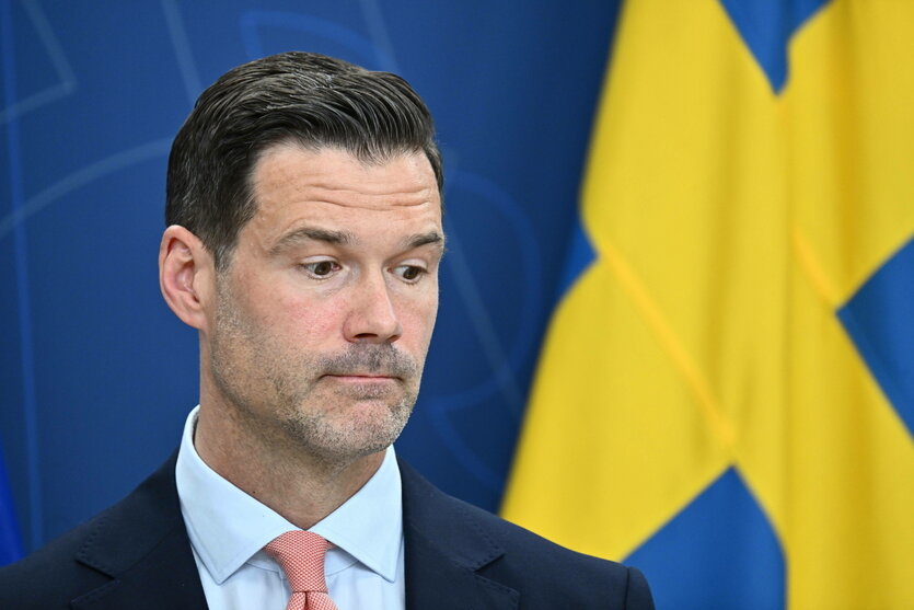 Ein Mann steht vor einer schwedischen Flagge und schaut skeptisch