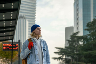 Ein sorgloser Hipster in stilvollem Outfit mit bunten Accessoires wartet auf die Tram