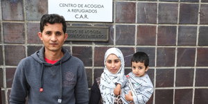 Ein Mann steht mit seiner Frau und Kind vor einer spanischen Flüchtlingsaufnahmestelle