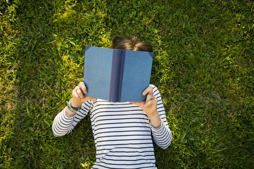 Ein Kind liegt auf einer Wiese und liest ein Buch