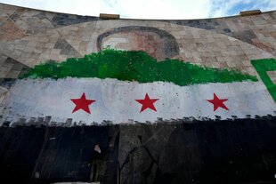 Ein syrischer Junge steht unter einem riesigen Porträt des verstorbenen syrischen Präsidenten Al-Assad, übermalt mit den Farben der sogenannten "revolutionären" Flagge