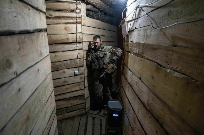 Ein ukrainischer Soldat telefoniert in einem Unterstand der aus Holzpaneelen gezimmert wurde