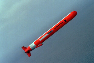 Eine orange Tomahawk Rakete fliegt quer durch Bild, im Hintergrund das Meer