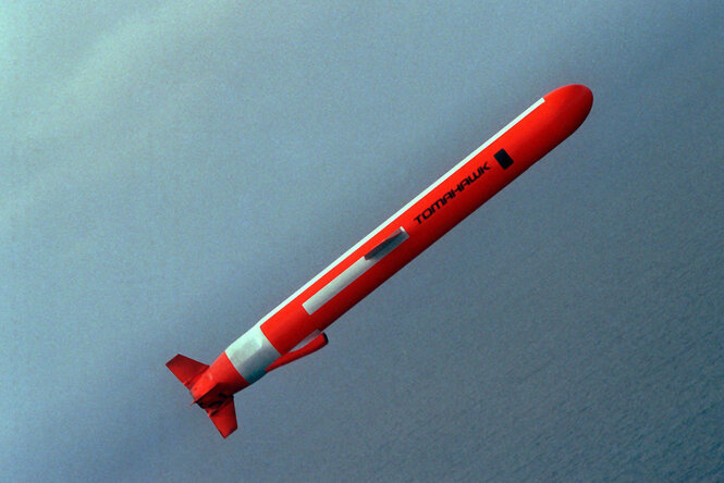 Eine orange Tomahawk Rakete fliegt quer durch Bild, im Hintergrund das Meer