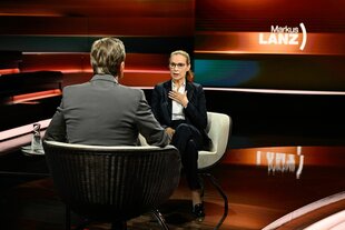 Eine Frau in einem Fernsehsstudio, davor ein Mann mit Rücken zur Kamera