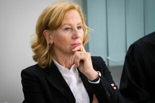 Eine Frau in schwarzem Jacket hält eine Hand an ihr Kinn und schaut skeptisch