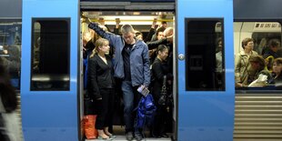 Menschen, dichtgedrängt, in einer Bahn, die Tür steht offen.