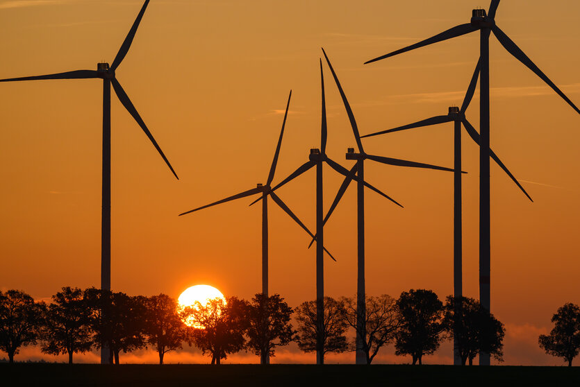 Die Sonne geht hinter Windenergieanlagen in Brandenburg auf