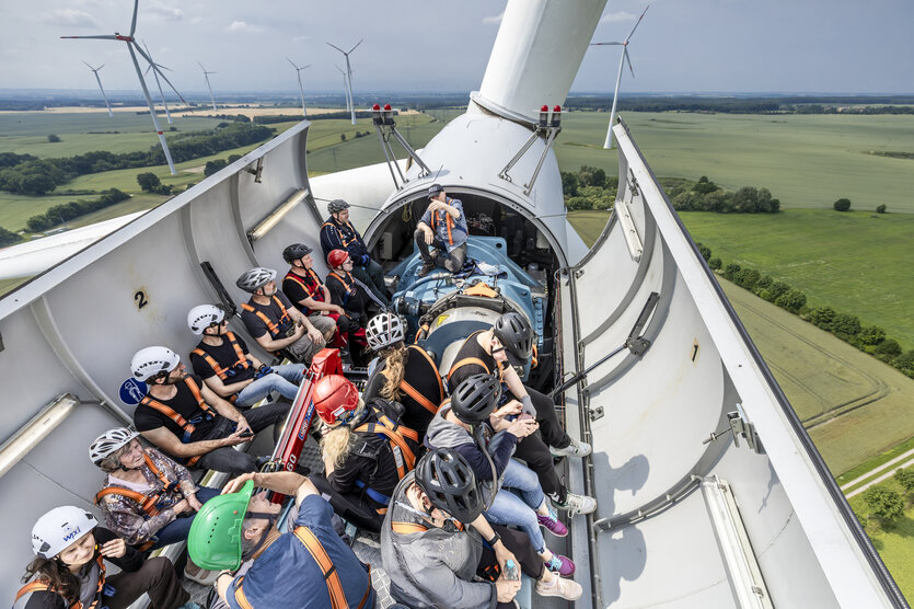 Eine Menschegruppe sitzt im offenen Maschinenhaus einer vorübergehend abgeregelten Windkraftanlage in 80 Meter Höhe